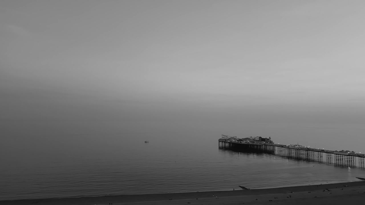 Brighton West Pier shoreline showing remaining pier structure extending over calm sea with pebble beach and overcast sky along Brighton coast in England