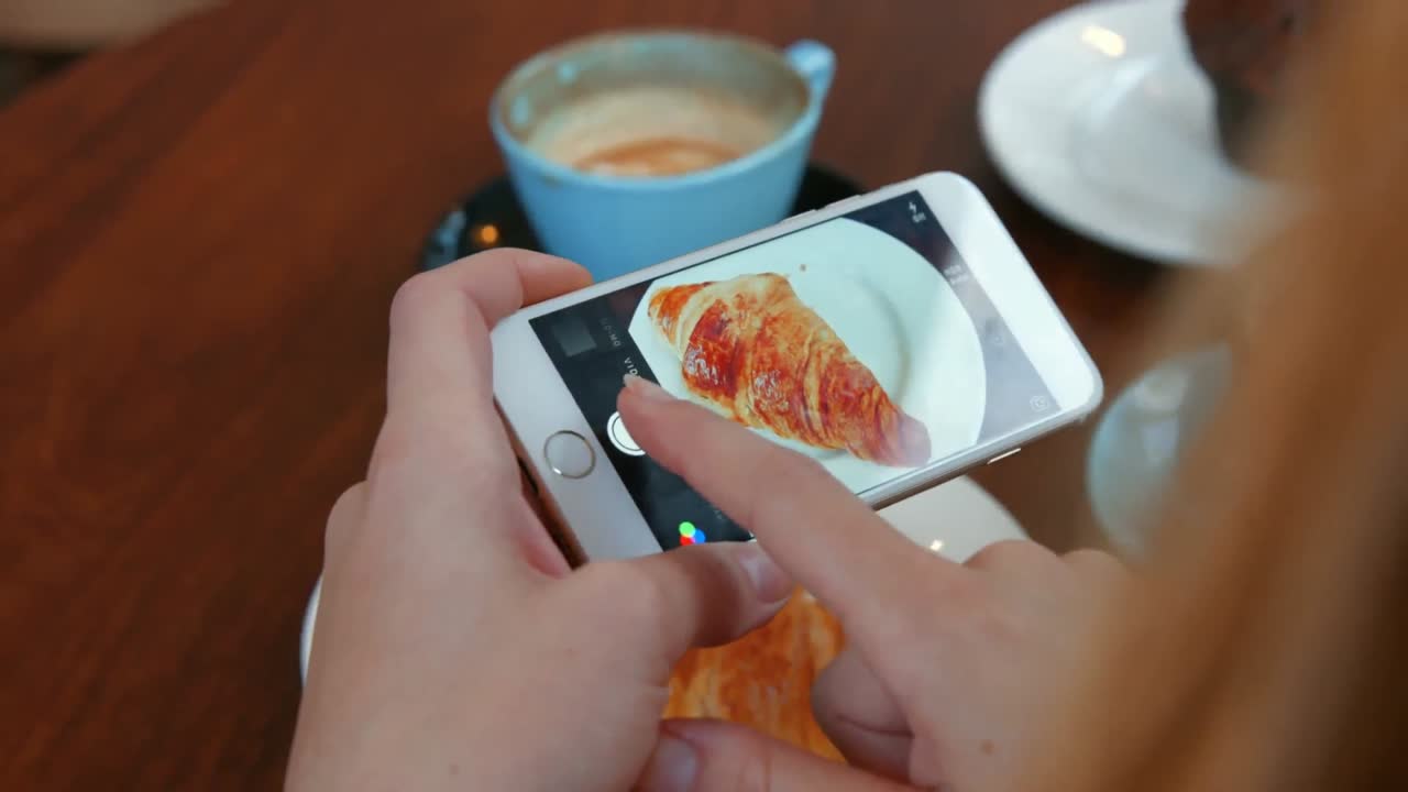 mujer fotografiando su croissant en un teléfono inteligente