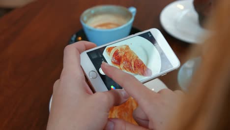 Woman-photographing-her-croissant-on-smartphone
