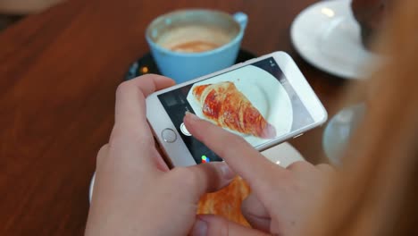 woman photographing her croissant on smartphone