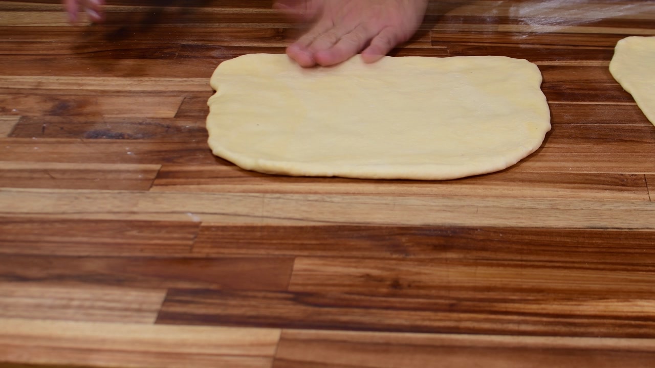 Dough sticks to rolling pin on wooden table while being stretched