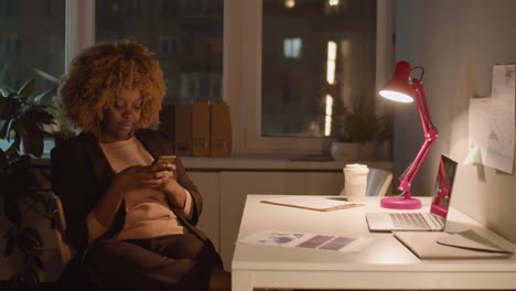 african american businesswoman using phone in office at night
