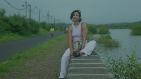 slow motion shot of a young indian woman dressed in an elegant purple dress, stands gracefully on the banks of a tranquil river