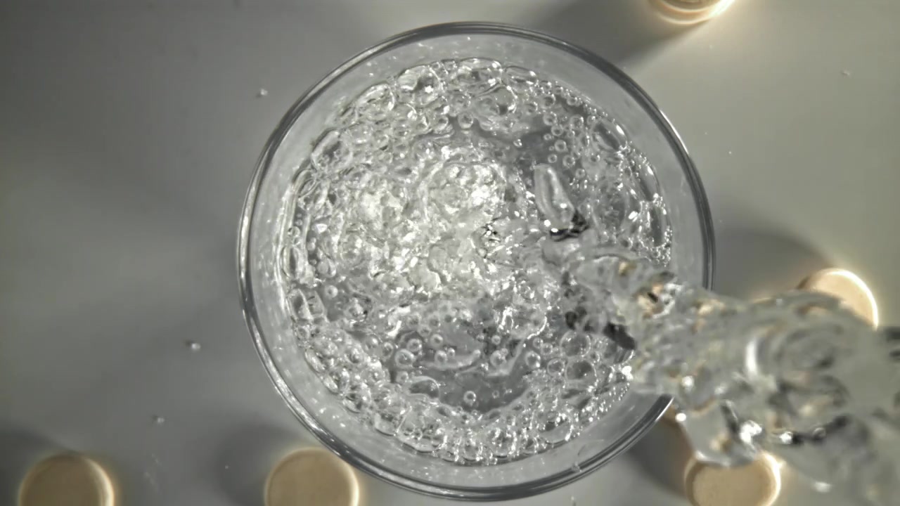 Acqua versata al rallentatore in un bicchiere con compresse effervescenti