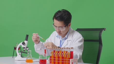 side view of asian man scientist making experiment with test tube and writing into notebook while working on the table with microscope in the green screen background laboratory