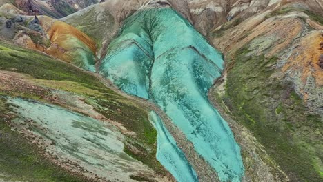 Drone-Aéreo-Con-Un-Rápido-Movimiento-Hacia-Atrás-Y-Un-Lento-Deslizamiento-Hacia-Abajo-Sobre-Grænihryggur,-La-Roca-Verde,-En-Landmannalaugar,-Islandia,-Enfatizando-Los-Tonos-Medios-De-Naranja-Y-Verde.