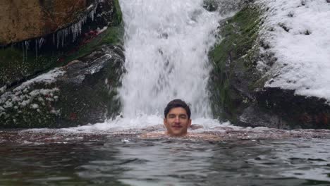 gelo masculino adulto nadando em água gelada sob uma cachoeira pitoresca nas montanhas durante o dia de inverno - tiro estático, câmera lenta