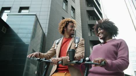 hombre y mujer afroamericanos de pie con scooters eléctricos y charlando