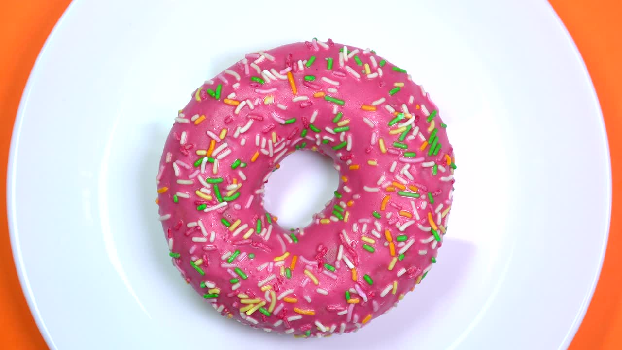 brillantes y coloridas salpicaduras de rosquilla, tiro macro, girando lentamente en un plato sobre un fondo naranja.