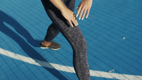 close up of a sporty woman warming up legs at sport court in sunlight on a summer morning