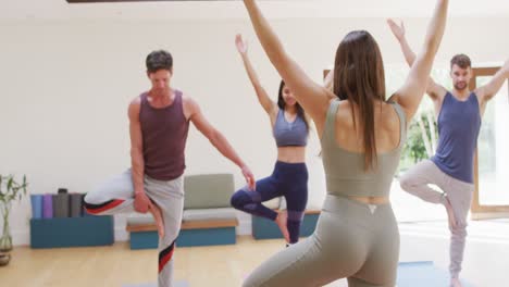 Caucasian-female-yoga-instructor-demonstrating-position-to-diverse-group-during-yoga-class-at-studio