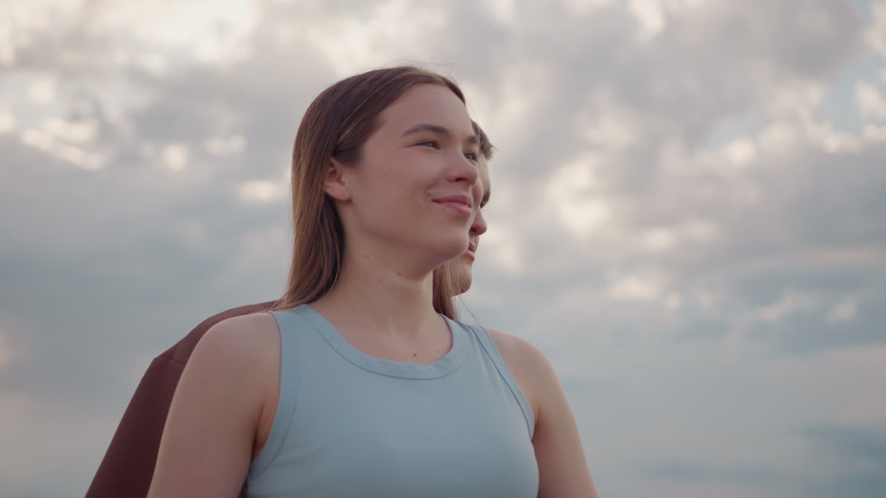 Warm moment captured as man approaches smiling woman from behind on open field with dramatic clouds above, highlighting calm affection, connection, and emotional expression