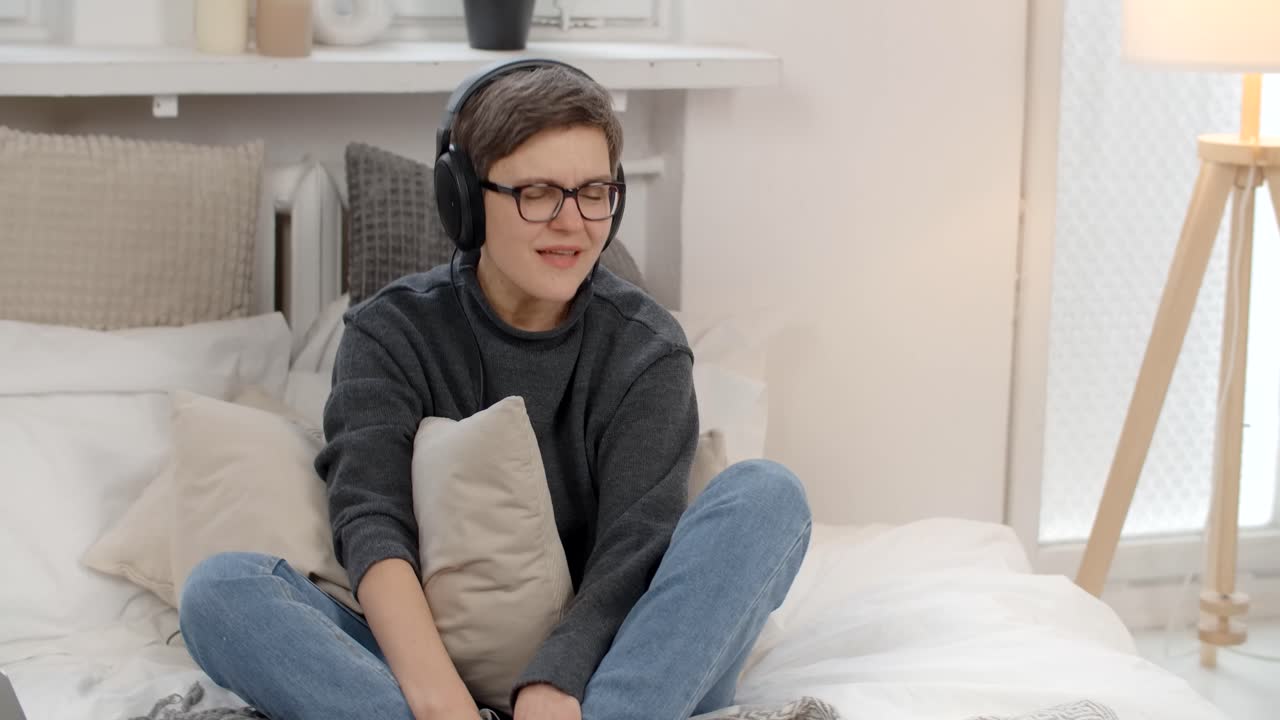 Woman listening to music on headphones in a bedroom