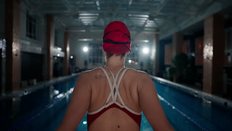 a woman in a red swimsuit stands at the edge of a swimming pool