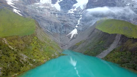 aéreo, reverso, disparo de drones inclinándose sobre el lago laguna humantay, en las montañas de los andes, día nublado, en la región de cusco, perú