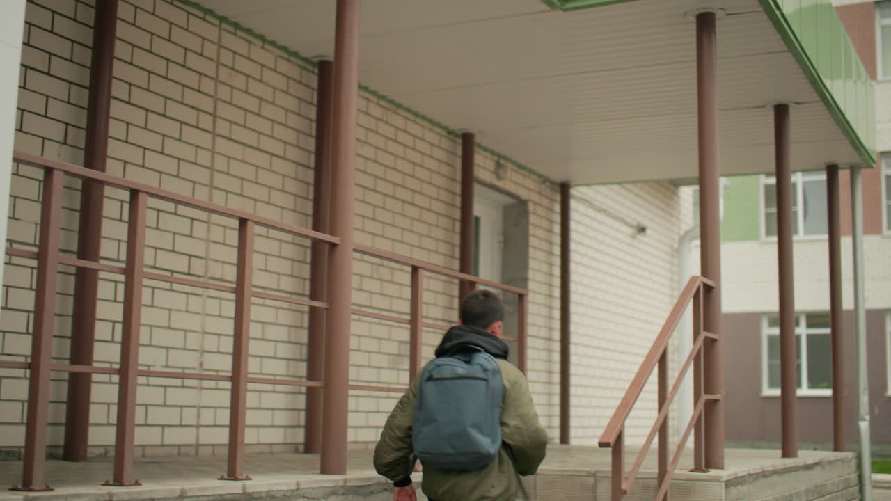 Vista trasera de un estudiante con mochila corriendo rápidamente hacia la entrada de la escuela, subiendo escalones con determinación en un día nublado, representando la vida académica y la energía juvenil