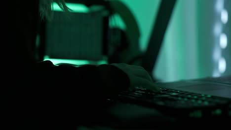 uma hackergirl criminosa com capuz preto usando laptop e grandes computadores para hackear o sistema de rede de sua sala escura de neon hacker