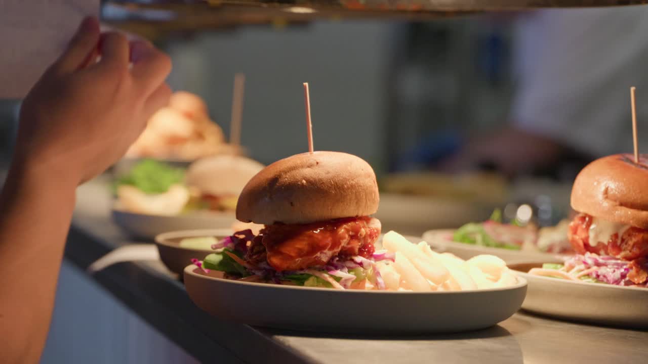 A restaurant pass lined with meals, ready and waiting to be taken to customers. A waiter steps in, lifts the plates and docket, and carries them away