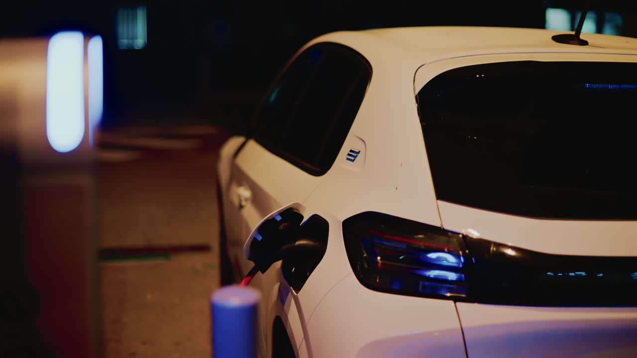Vista posteriore di un'auto elettrica bianca collegata a un caricabatterie da strada di notte