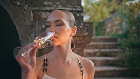 una mujer elegante bebiendo vino blanco en un hermoso palacio abandonado de cerca.