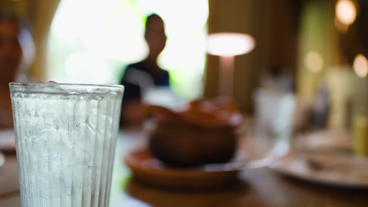 Hand serves hot clay pot soup to diners in warmly lit Bangkok restaurant, shallow focus