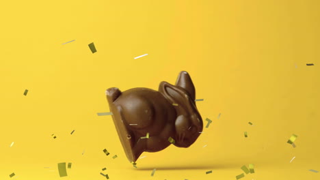 animación del conejo de pascua de chocolate cayendo y confeti dorado volando sobre un fondo amarillo