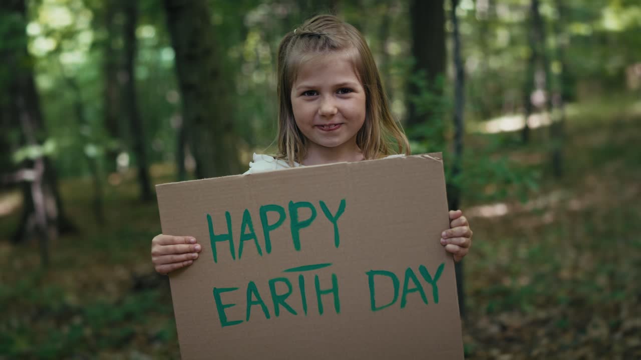 숲에서 포스터를 들고 미소 짓는 작은 소녀의 초상화.