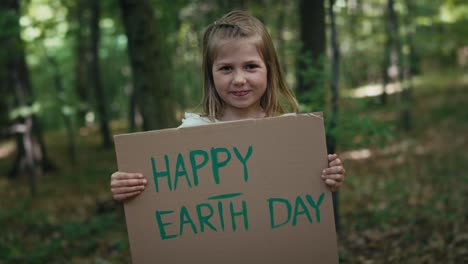 portrait of little girl smiling and holding poster in the forest.