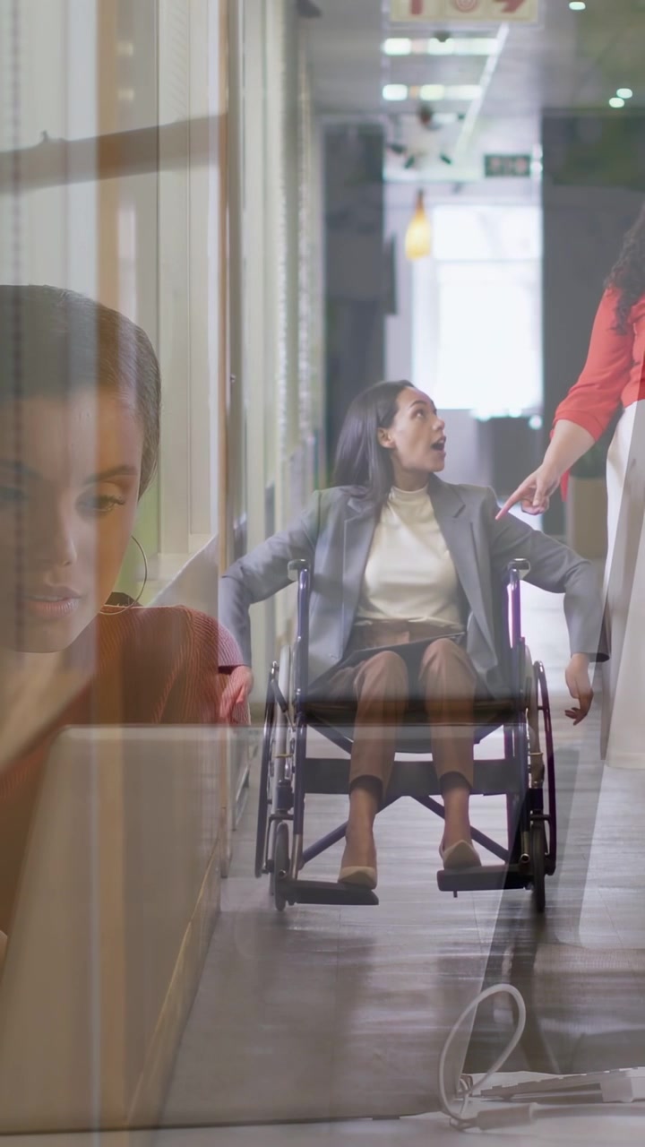 Video verticale: Donna che spinge una sedia a rotelle azionando i corrimano in ufficio, prestando attenzione a un collega che indica, con una sovrapposizione sfumata.