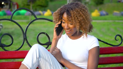 happy african woman talking on the phone while sitting on a bench in the park