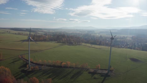 Windkraftanlagen-An-Einem-Sonnigen-Tag-In-Der-Nähe-Des-Dorfes,-Umgeben-Von-Einer-Wiese