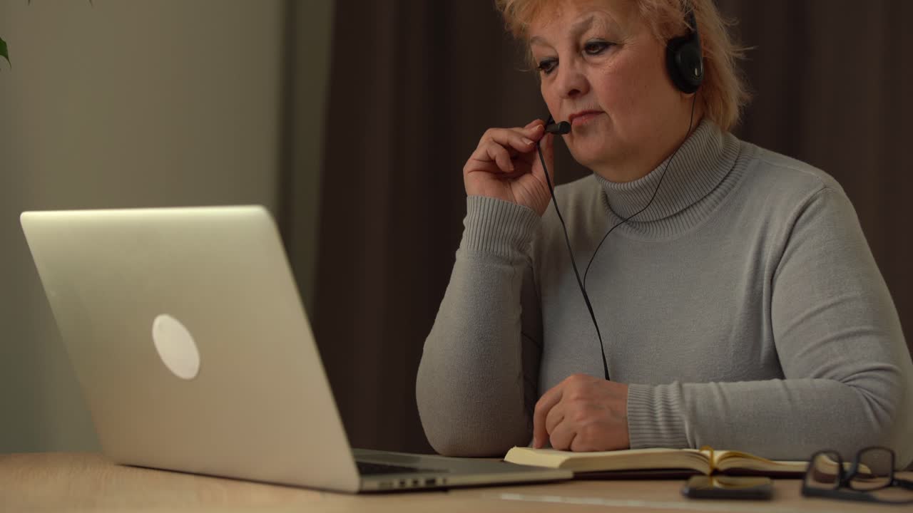 Senior female teacher in headset giving online lesson on laptop