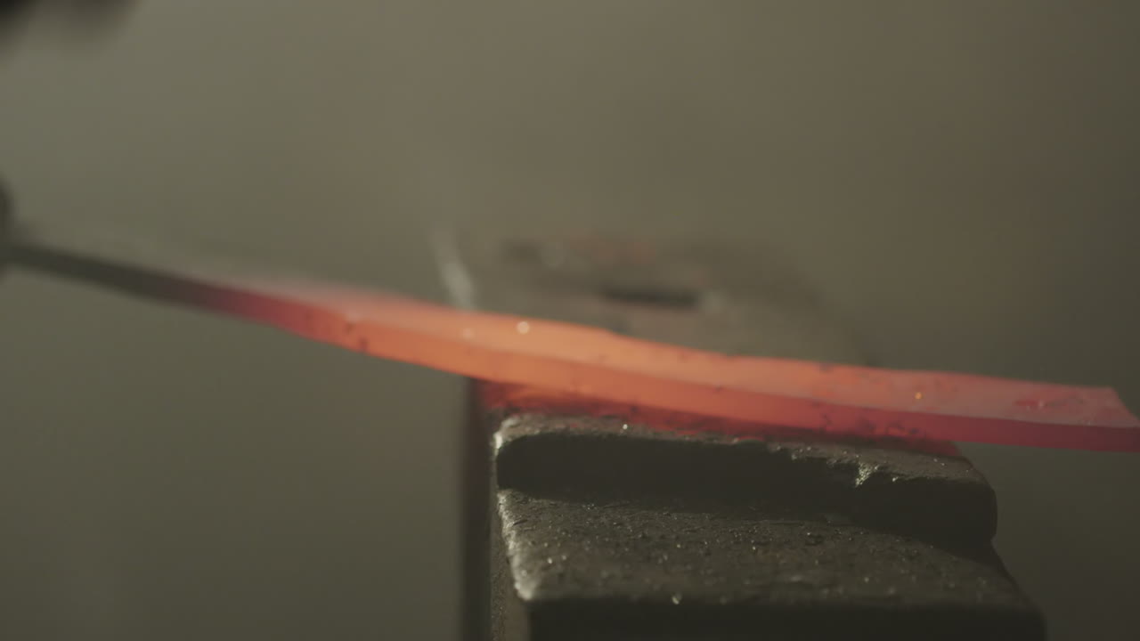 A blacksmith beats a hot piece of metal with a hammer