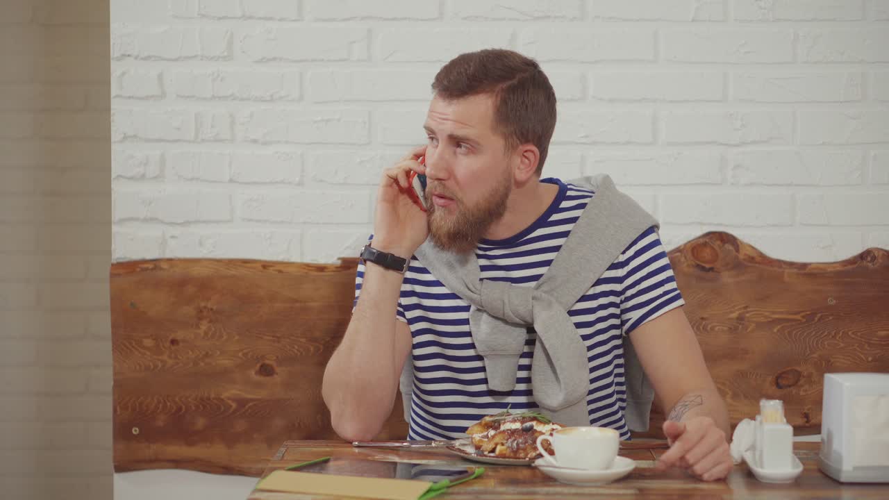 hombre hablando por teléfono mientras come el desayuno en una cafetería