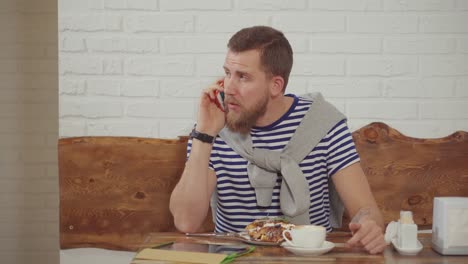 man talking on phone while eating breakfast in cafe