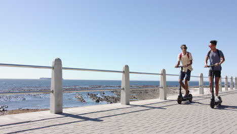 happy diverse gay male couple using scooters at promenade by the sea, slow motion