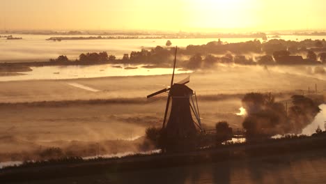 sunrise over dutch landscape with a windmill in a foggy morning