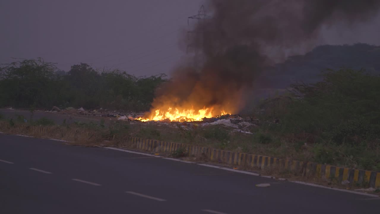 Trash burning and spreading poisonous black smoke at side of a road in india