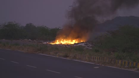 trash burning and spreading poisonous black smoke at side of a road in india