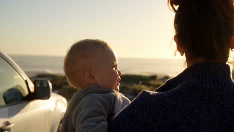 Madre-Sosteniendo-A-Su-Bebé-Cerca-De-La-Playa-4k