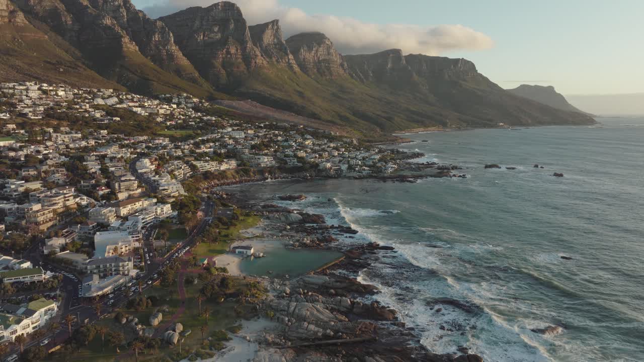 Drone flies over camps bay in cape town south africa - many houses on a hillside - drone flies over the bay with view to table mountain and rocks in the sea
