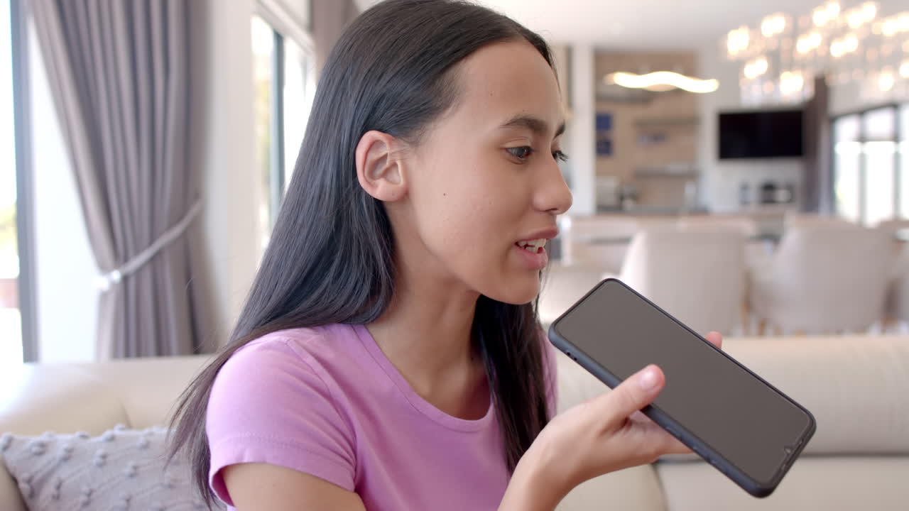 Biracial teenage girl holding smartphone, talking at home