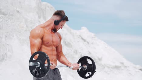 a man in headphones does barbell biceps exercises. workout in nature