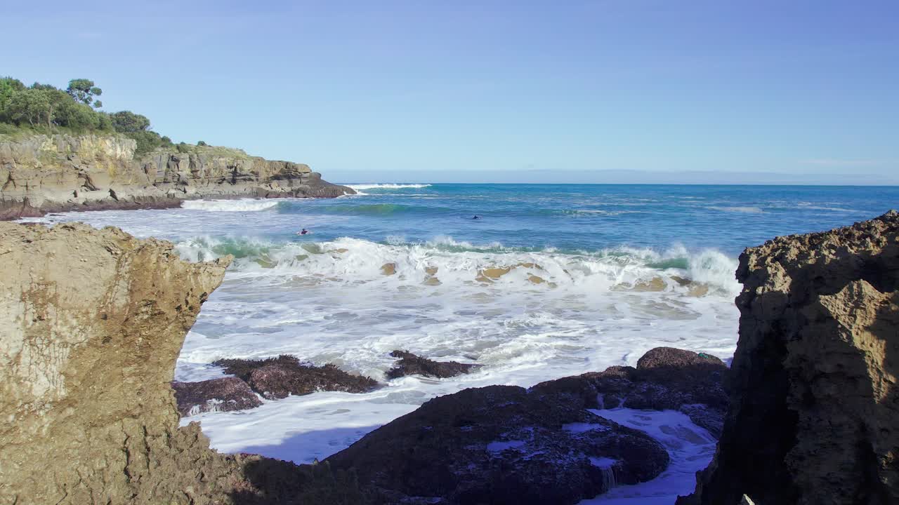 Aerial push in shot between rocks in of the waves in the shore in Cantabria, Spain on a sunny day