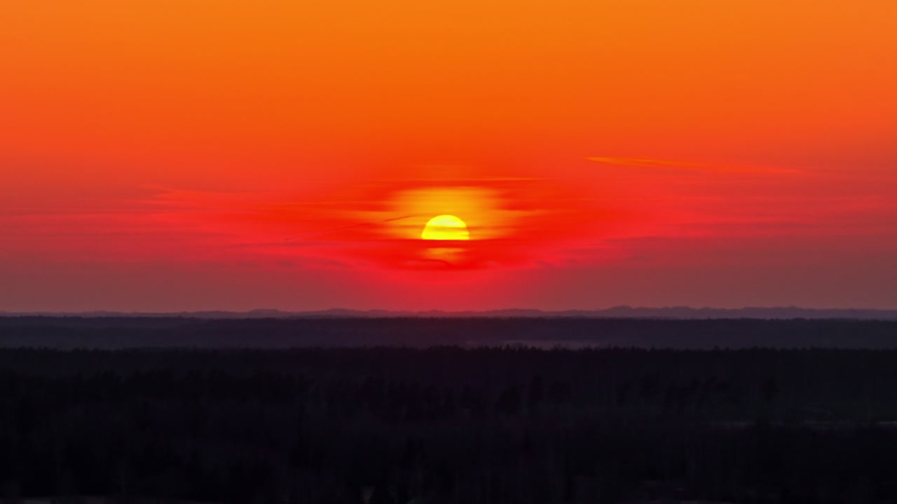 Sun setting creating a warm glow with orange sky above the horizon and dark landscape, aerial natural background