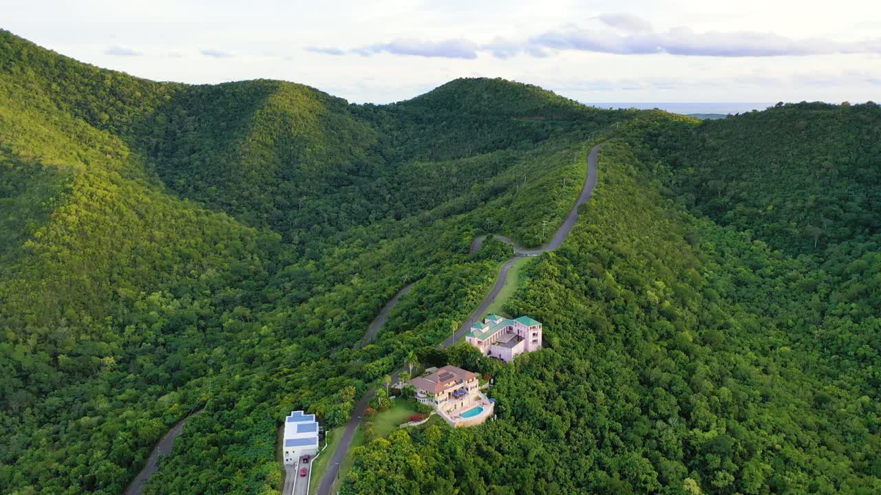 Drone view of St. Croix captures upscale villas tucked quietly in green forested hills, with tall trees, gentle island slopes, and distant mountain peaks rising beneath a flawless Caribbean sky