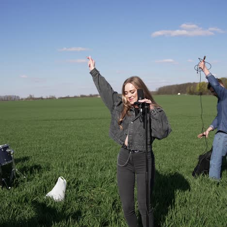 energetic and cheerful musicians perform music on green field. young band singing and dancing outdoors. men and a woman play drums and sing a song into a microphone