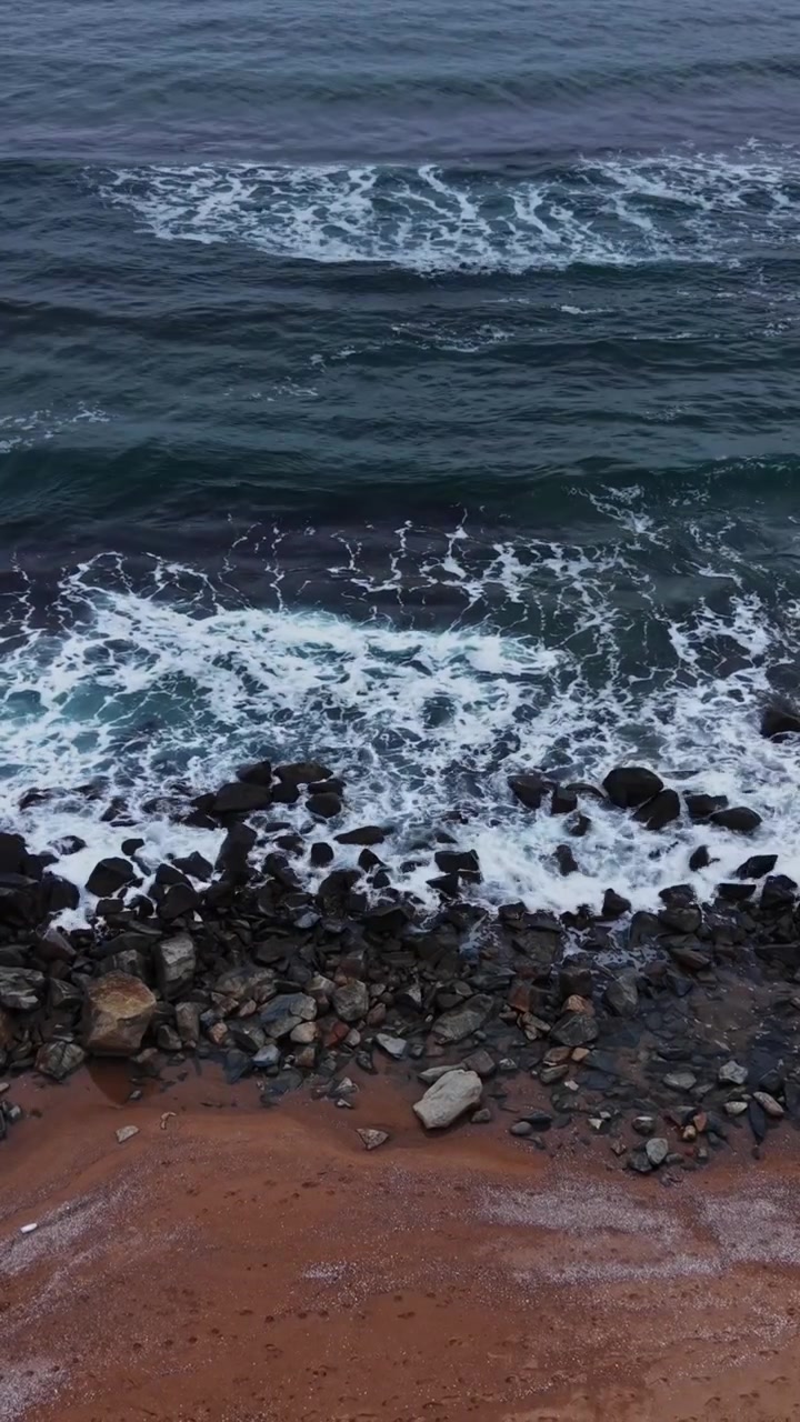 Onde che si infrangono sulla costa rocciosa vicino alla spiaggia sabbiosa durante un pomeriggio nuvoloso