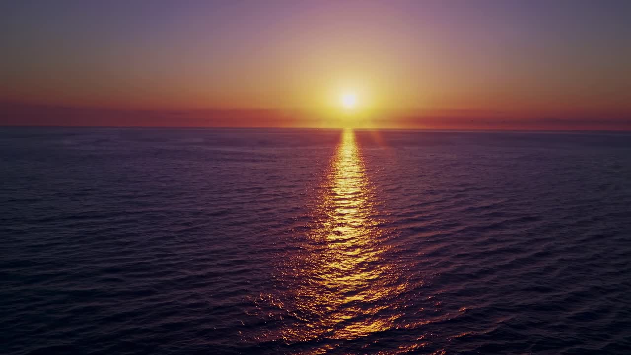 Aerial video captures a serene ocean sunset, with the sun's reflection creating a golden path