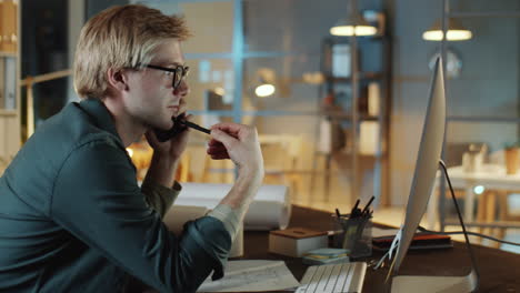 architect talking on phone and working on computer in night office